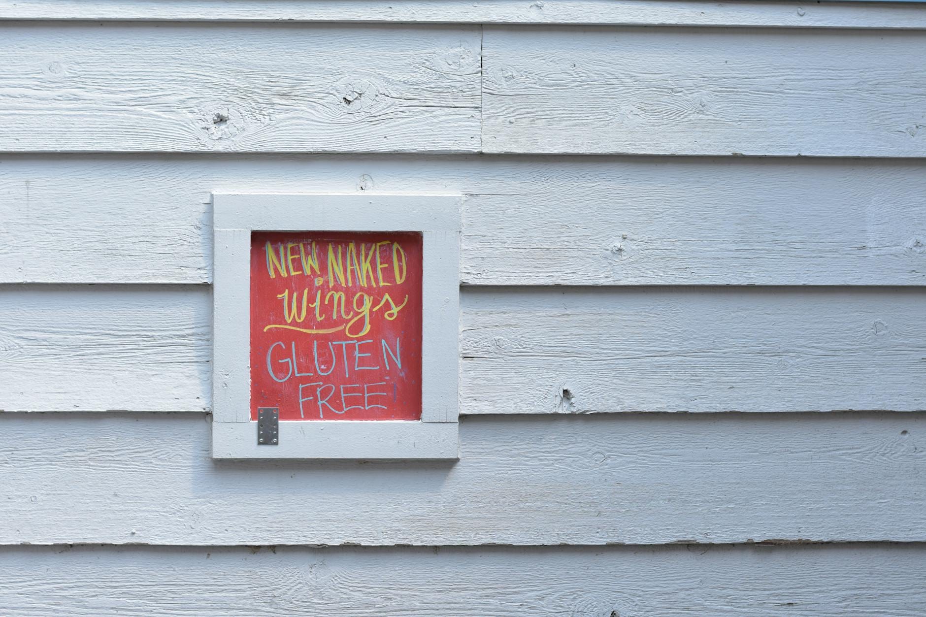 Kolorowy szyld z napisem bezglutenowe skrzydełka na białej ścianie