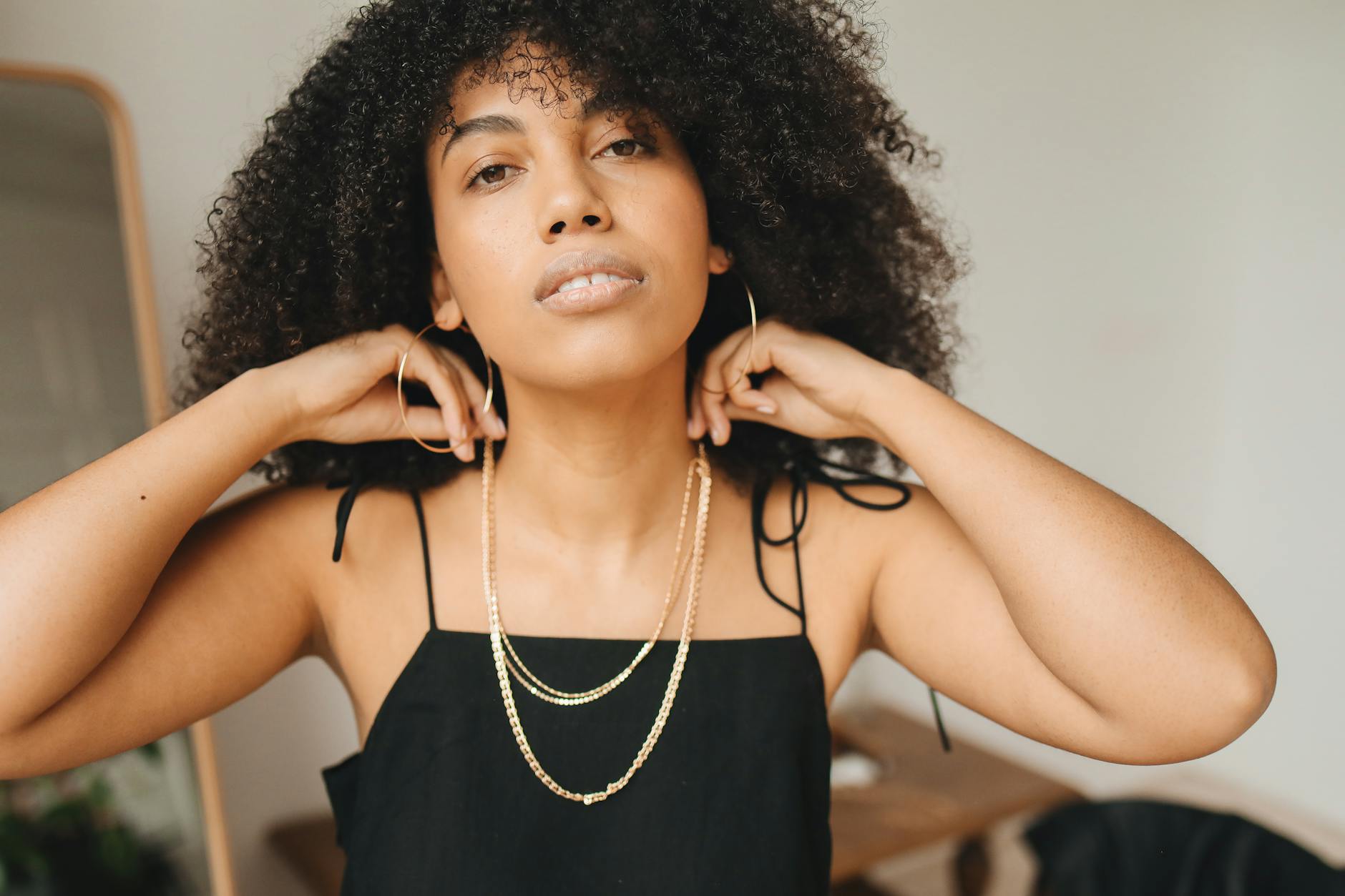 Kobieta w czarnej sukni glamour poprawia złotą biżuterię w eleganckim wnętrzu