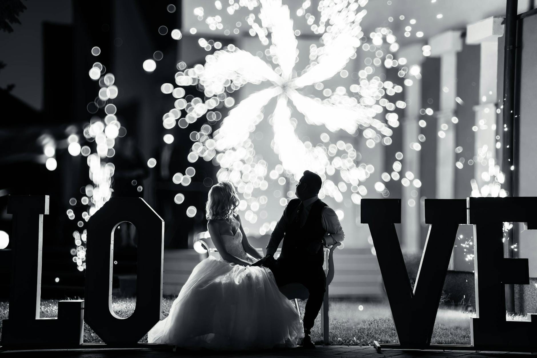 Para młoda ogląda nocne fajerwerki obok świecącego napisu LOVE