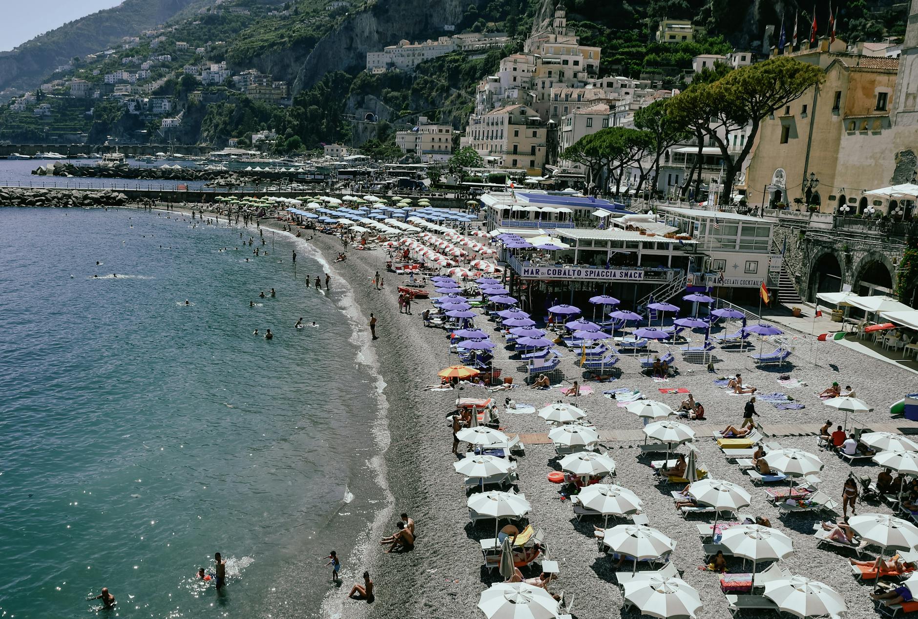 Tłoczna kamienista plaża w Amalfi z kolorowymi parasolami i leżakami