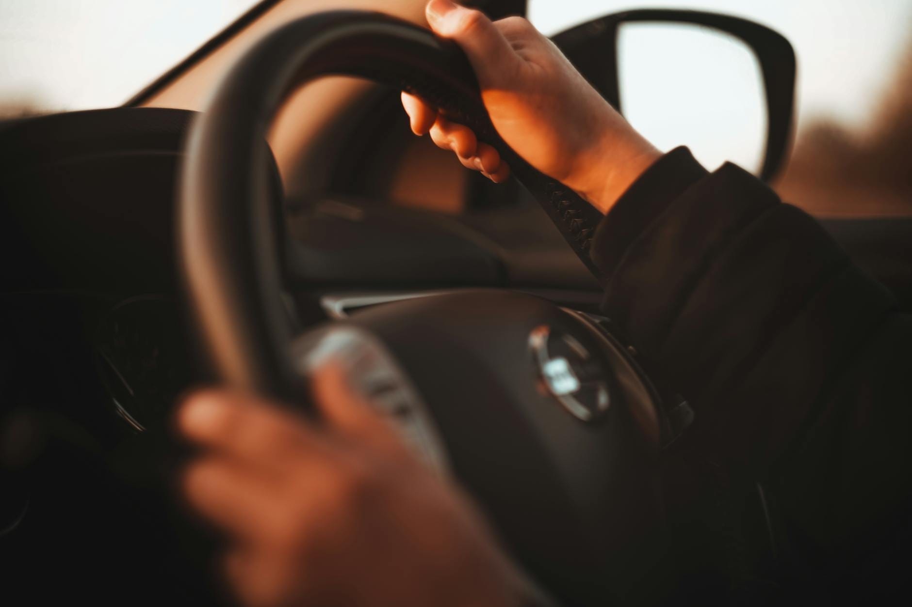 Dłonie kursanta pewnie trzymające kierownicę w świetle zachodu słońca