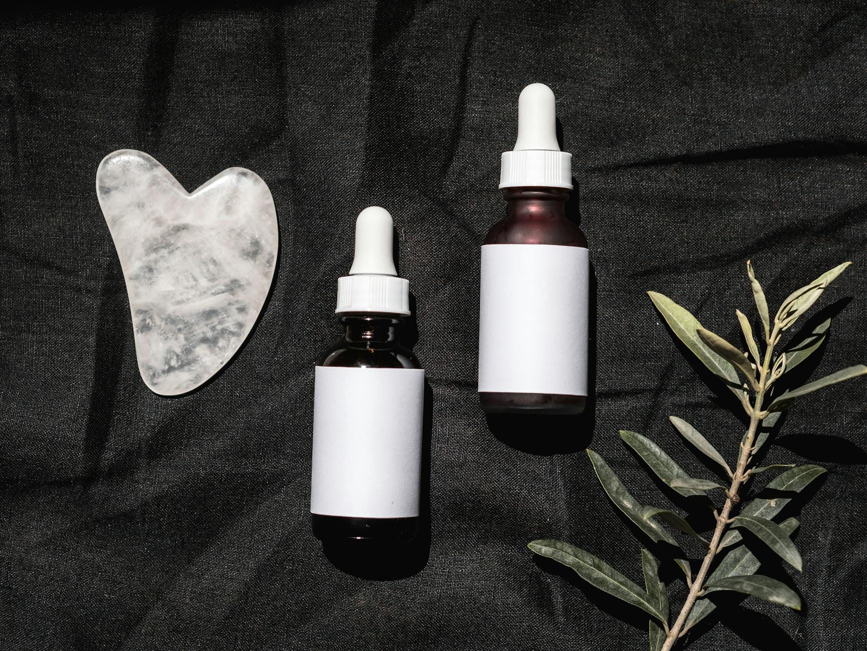 Minimalistyczny flatlay buteleczek do pielęgnacji, gua sha i gałązki na ciemnym