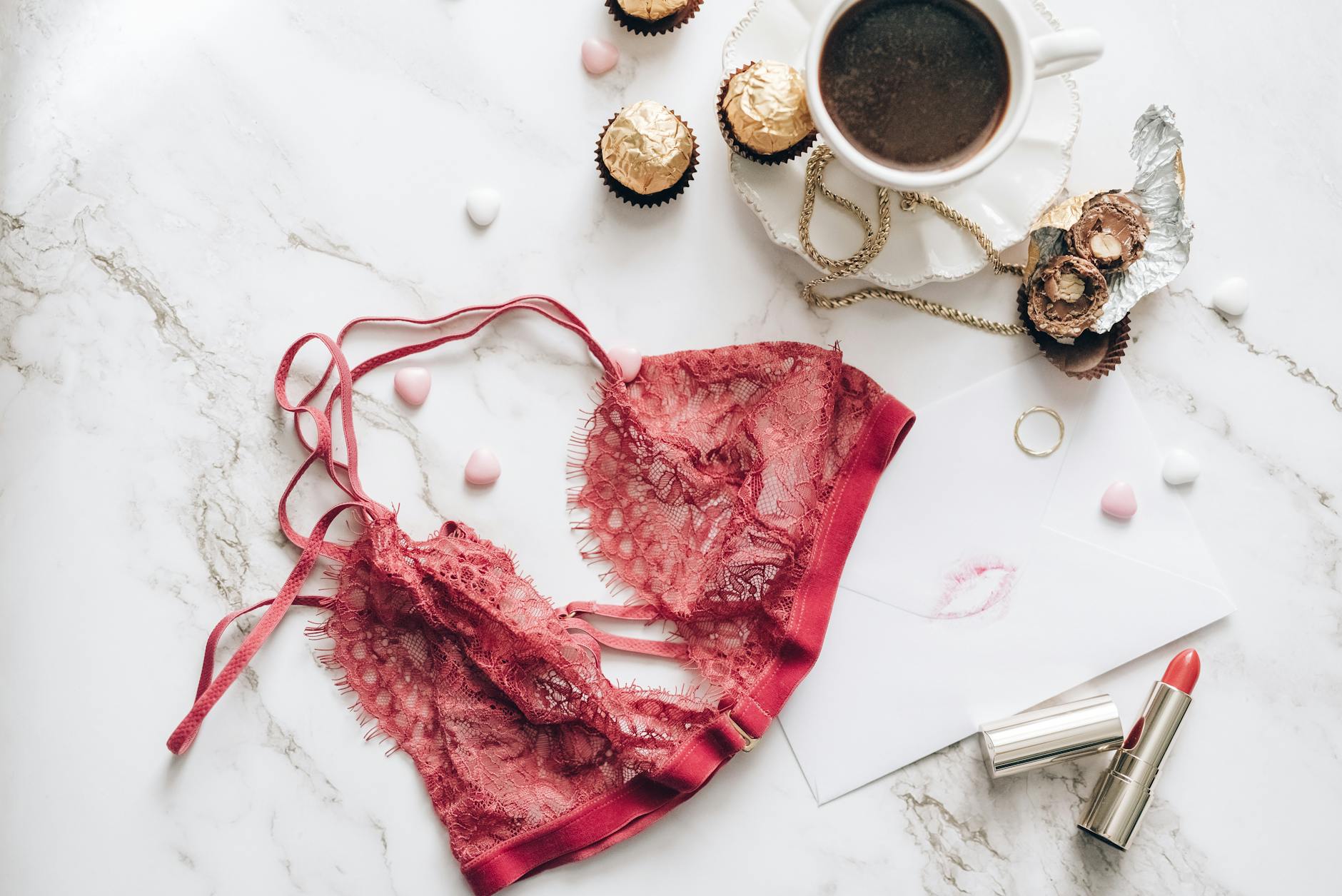 Czerwone koronkowe lingerie, kawa, czekoladki i szminka na marmurze