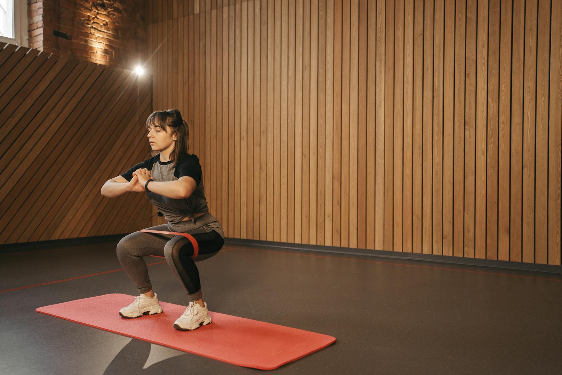 Młoda kobieta ćwiczy w domu z gumą oporową na macie fitness Młoda kobieta ćwiczy w domu z gumą oporową na macie fitness