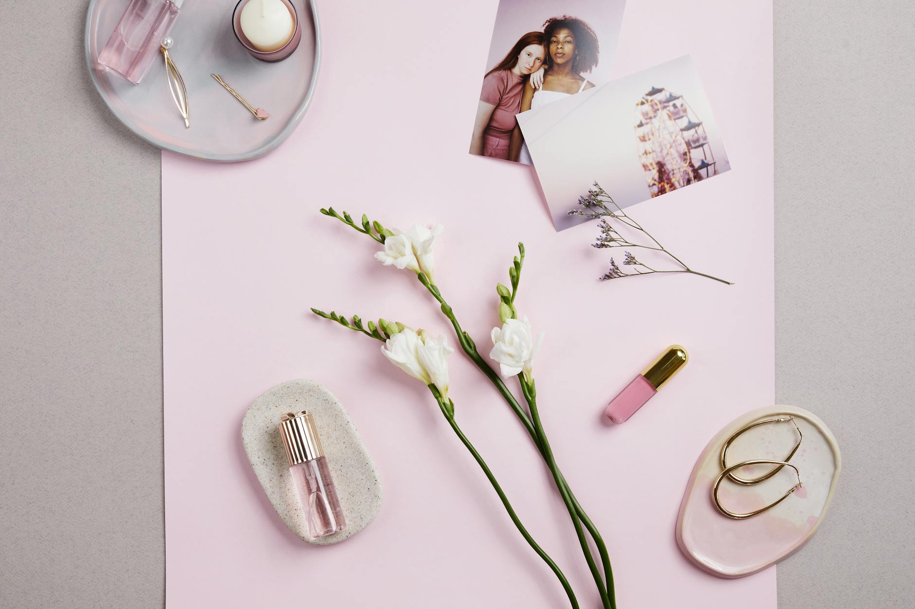 Perfumy, kolczyki i kwiaty w stylowym flat lay na różowym tle
