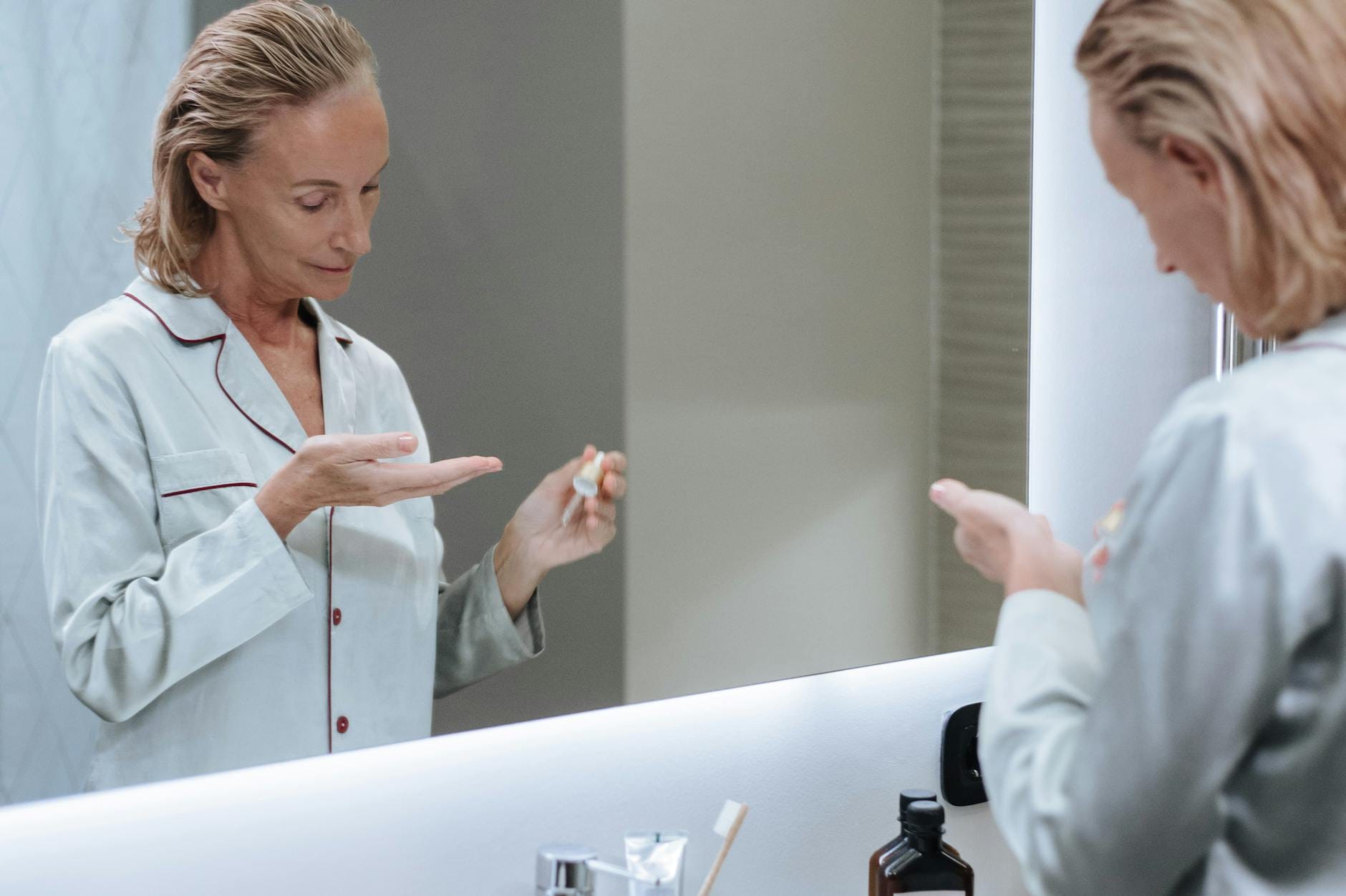 Starsza kobieta nakłada serum na twarz przed lustrem w łazience