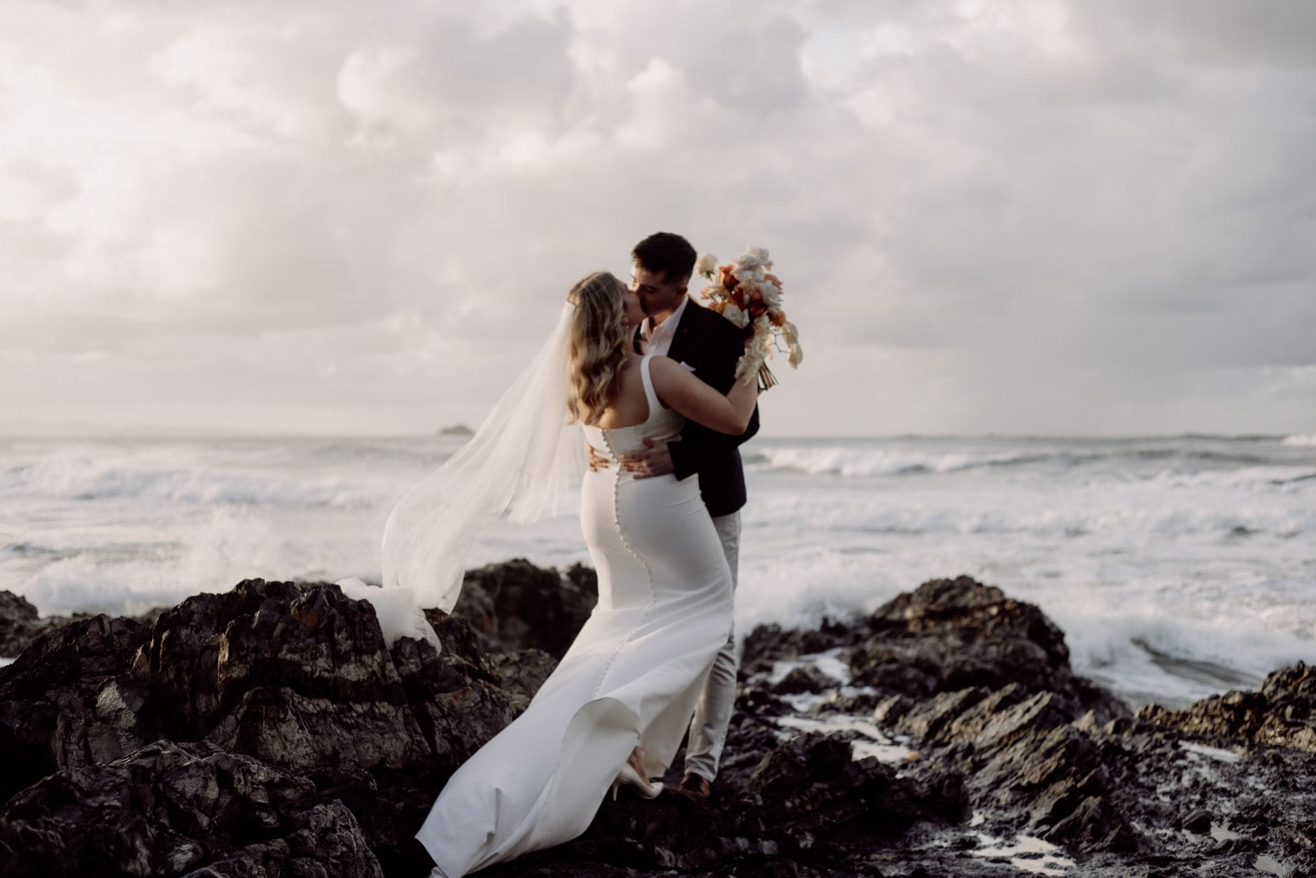 Nowożeńcy całują się na skalistym wybrzeżu w Byron Bay
